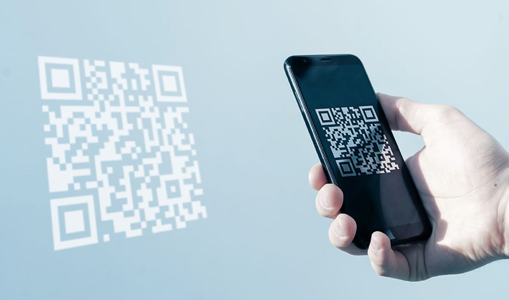 Mão de uma pessoa segurando um celular fazendo a leitura do QR Code na parede